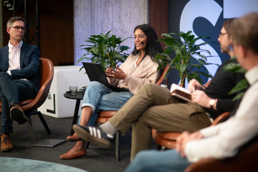 Panelisti Moshumee Dewoo puhuu ja elehtii nojatuolissa muiden keskustelijoiden kuunnellessa.